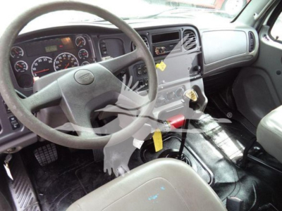 Dashboard and steering wheel of a 2006 Freightliner Business Class M2 106 interior with gray seats and manual transmission shifter visible.