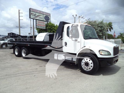 Truck image of a white Freightliner Business Class M2 106 rollback with a long flatbed chassis and dual rear axles.