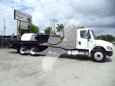 Truck shows Freightliner Business Class M2 106 rollback w/ flatbed. Side view of white cab, black flatbed, and fuel tanks visible.