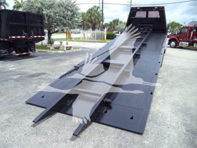Truck bed with a raised flatbed incline and wheel-lift ramps, black metal surface, Freightliner M2 106 rollback equipment visible.