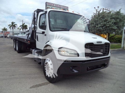 Truck bay showing 2006 Freightliner Business Class M2 106 with a flatbed/dolly tow setup, white cab, black grille, dual rear axles, daytime outdoor lot.