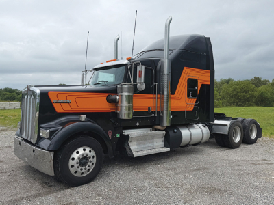 Kenworth W900L AeroCab tractor truck side view showing black and orange paint, large exhaust stacks, chrome bumper, dual rear axles, and fuel tanks.