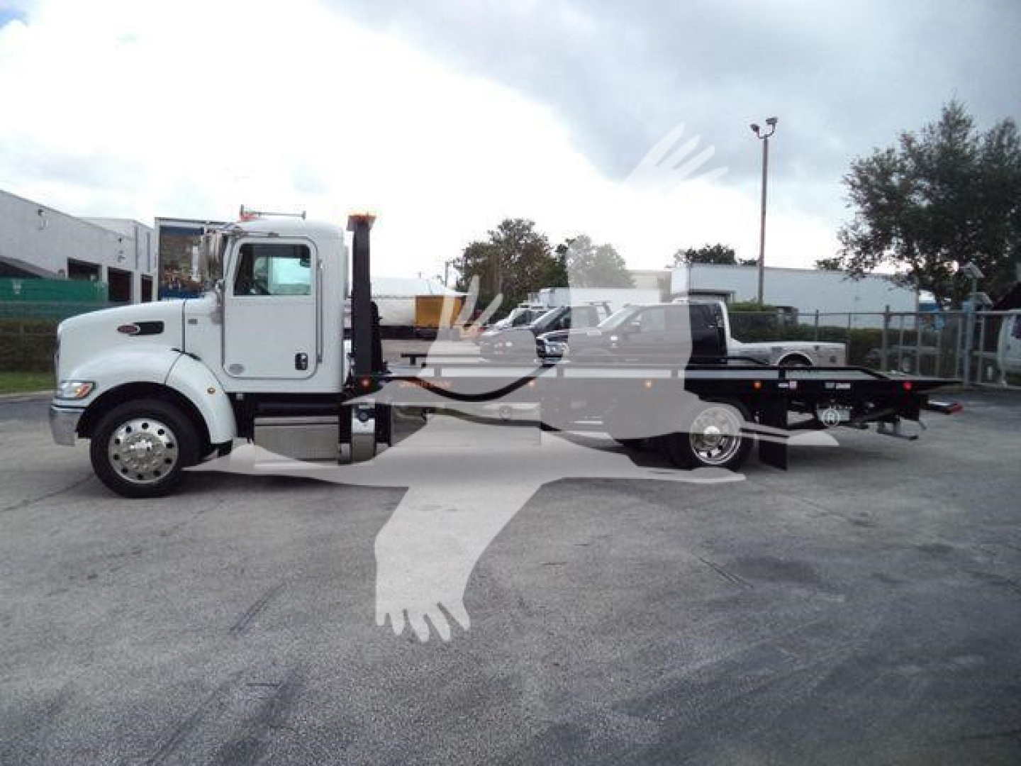 Truck cab with rollback tow in a parking lot showing Peterbilt 337 side view and flatbed tow rear