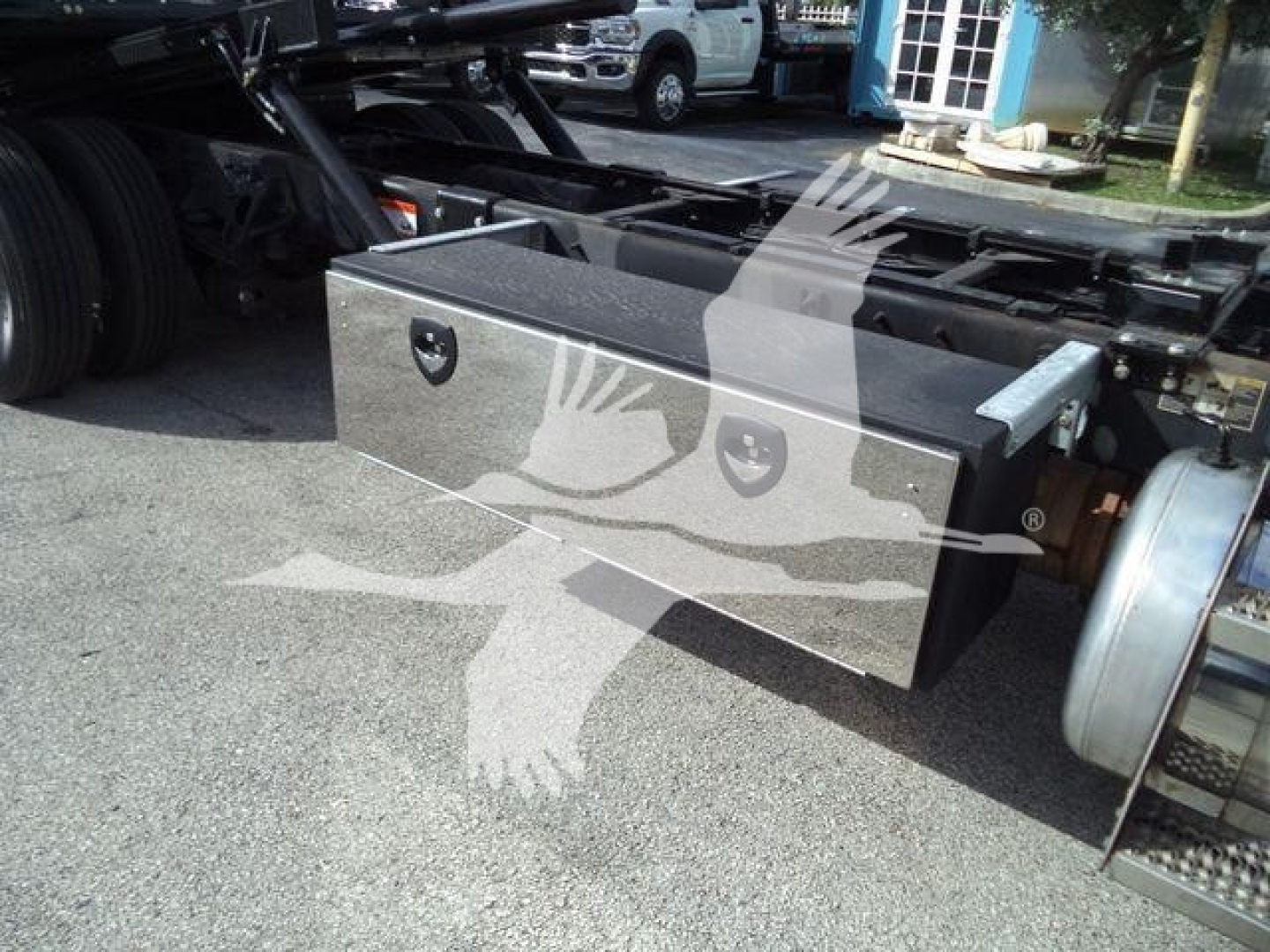 Rectangular metallic toolbox mounted under a Peterbilt 337 chassis, with diamond-plate surface and two circular locking handles visible on the front face.