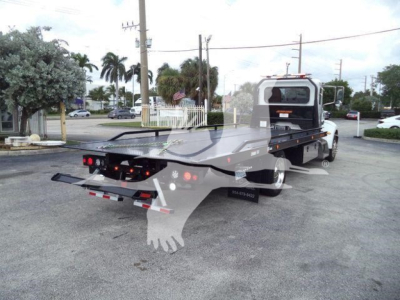Flatbed rollback tow truck with extended rear deck; Peterbilt 337 chassis; visible rear lights and bumper; no legible text seen on the visible parts.