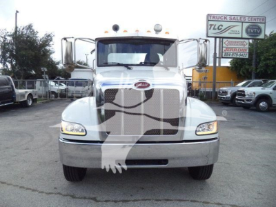 Truck front view of a 2019 Peterbilt 337 in a dealership lot, chrome grille and headlights visible, large bumper, sign in background.