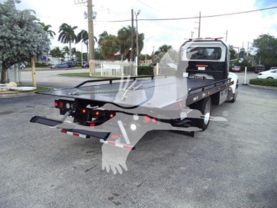 Truck bed of a rollback wrecker with a flatbed, rear view showing hydraulic launcher and rear lights.