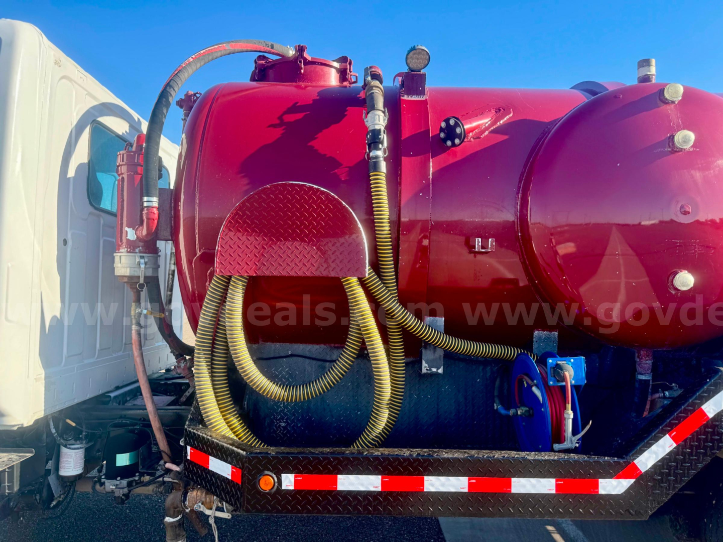 Hino vacuum tank truck side view with red cylindrical tank, hoses and controls mounted on a stake-bed chassis; stock number 24329-523 visible overall.