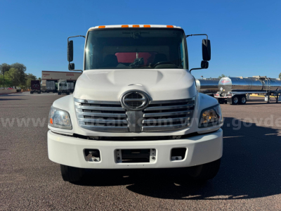 Front view of a white Hino vacuum tank truck with a large grille, dual mirrors, and a prominent Hino emblem on the grille. Headlights visible, front bumper with empty license plate area.
