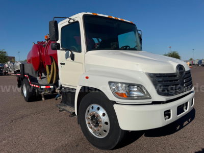 Hino vacuum tanker truck in white cab with red vacuum tank side view showing vacuum equipment and hose reel.