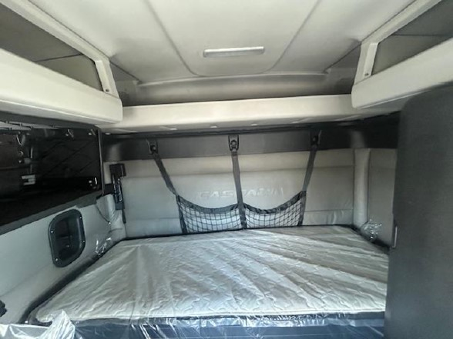 Cabin bunk area of a 2022 Freightliner Cascadia 116 sleeper showing a bed with white mattress and overhead storage shelves.