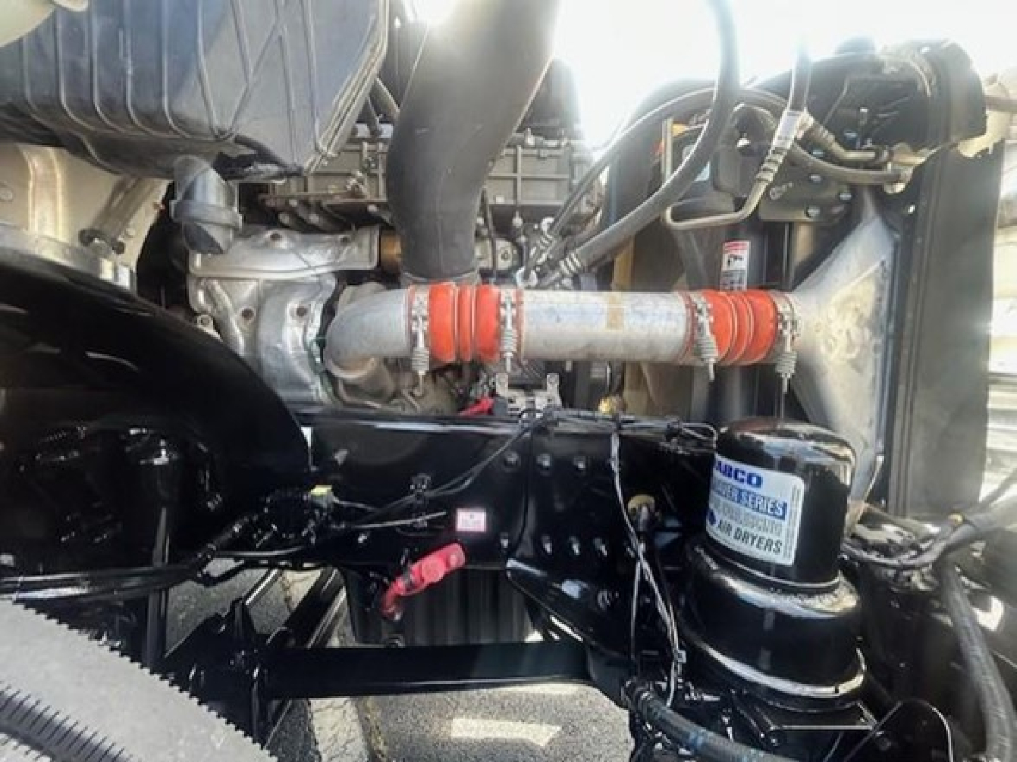 Engine bay of a Freightliner Cascadia showing hoses, belts, and a DPF-style compressor with a filter canister labeled not fully legible.