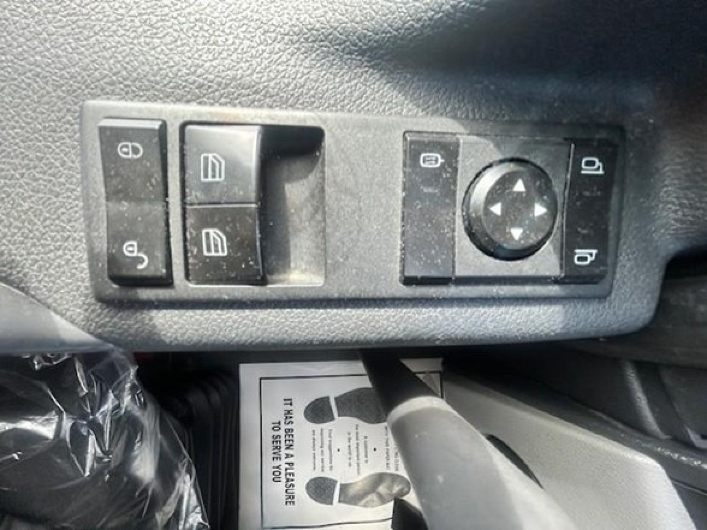Truck interior control panel with window/lock switches and circular joystick on driver door, plus a footwell card visible