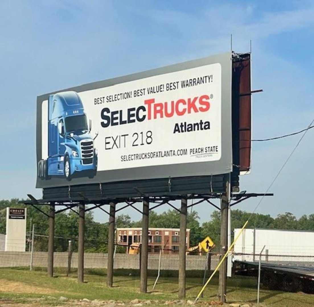 Billboard sign with blue Freightliner truck image and text 'SELECTTRUCKS Atlanta' and website info.