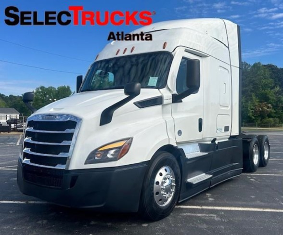 Truck cab exterior of a 2022 Freightliner Cascadia 116 in a dealership lot, white sleeper tractor with black bumper and chrome wheels.