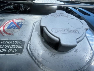 Diesel fuel cap and nearby labels visible in engine bay of a 2022 Freightliner Cascadia 116; circular cap with TURBO/990 markings and warning text.