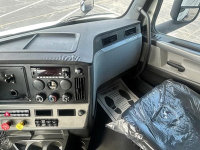 Freightliner Cascadia 116 truck interior dash area with steering wheel, control knobs, and plastic seat cover visible.