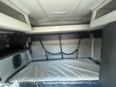 Cabin bunk area of a 2022 Freightliner Cascadia 116 sleeper showing a bed with white mattress and overhead storage shelves.