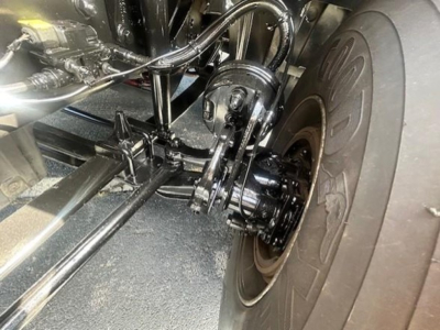 Freightliner Cascadia 116 truck front suspension and axle components visible; wheel and tire with dual steered axle, hydraulic lines, and frame members in view.
