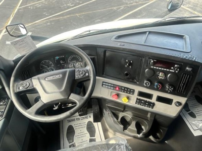 Interior of a Freightliner Cascadia cab showing steering wheel, dashboard with analog gauges, center console, and cup holders.