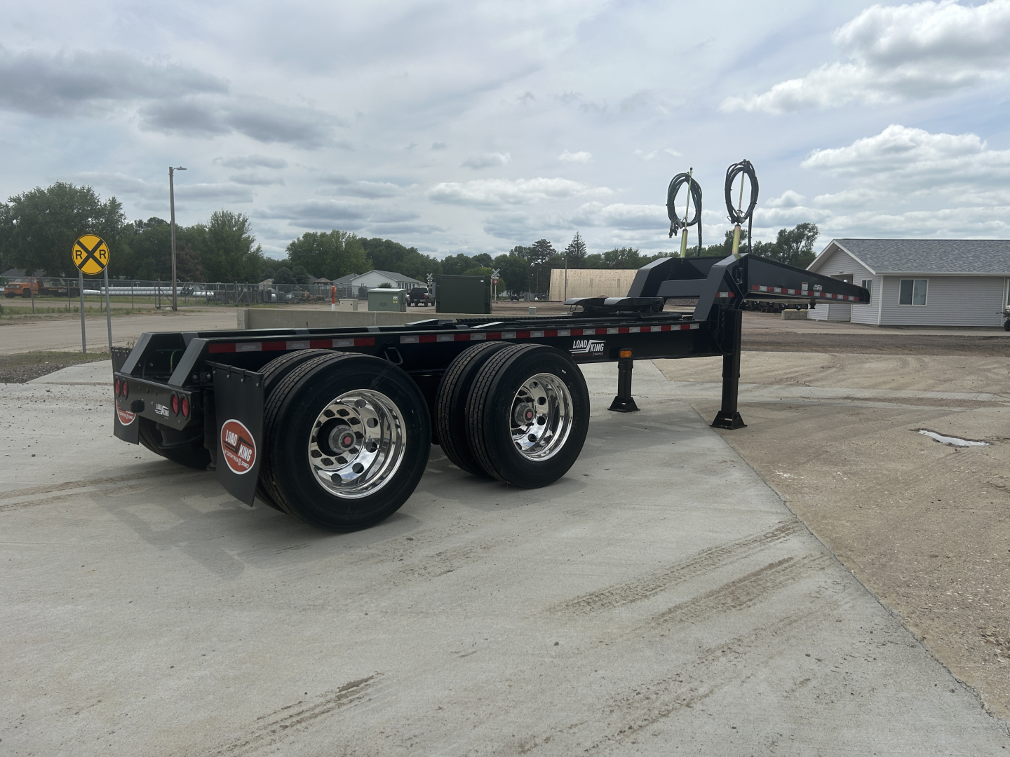 Load King HD702G trailer showing dual rear axles with chrome wheels and black steel framing; circular hoses mounted on upright posts; reflective tape and label decals on the side.