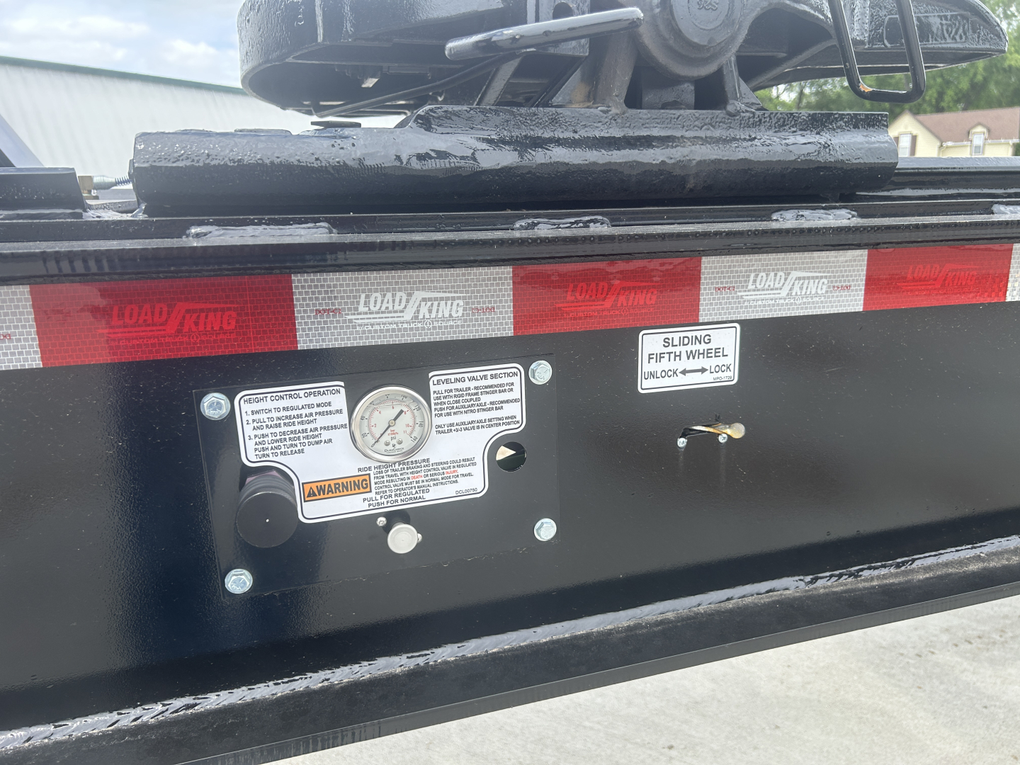 Load King HD702G trailer x-ray view showing control panel with labels, gauge, and warning stickers on black frame; red reflective tape along edge.
