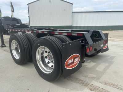 Load King HD702G trailer showing dual rear axles with large chrome rims and black mud flaps; rear frame and deck visible with reflective tape.