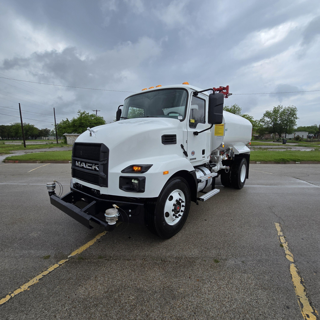 Mack MD7 cab and tank body in a parking lot, front-left view showing tanker apparatus and labels.