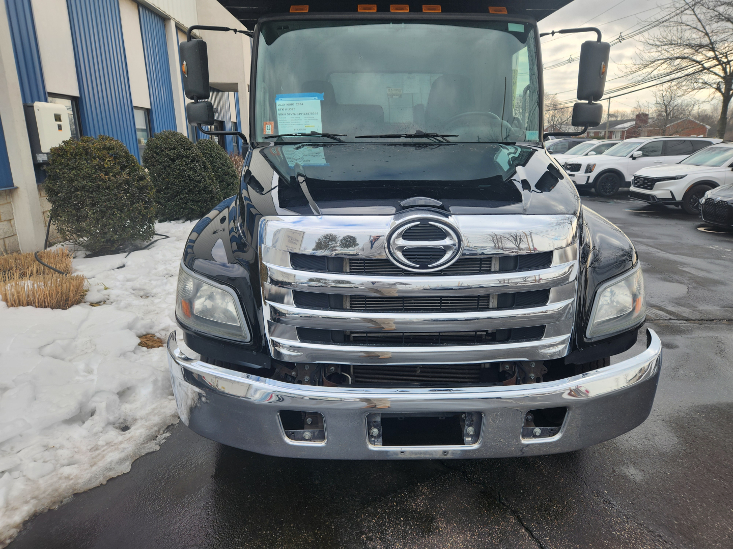 Front view of a black 2020 Hino 268A truck with chrome grille, headlights, and bumper; visible stock lot with other vehicles in background.