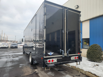 Rear view of a black box truck trailer attached to a 2020 Hino 268A, with dual rear doors and reflective surfaces.