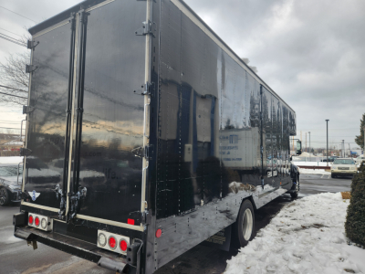 Black moving van trailer with rear doors and taillights visible in a parking lot.