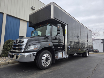 Truck cab and box truck in service showing Hino 268A moving van with dark container and chrome bumper; front grill visible.