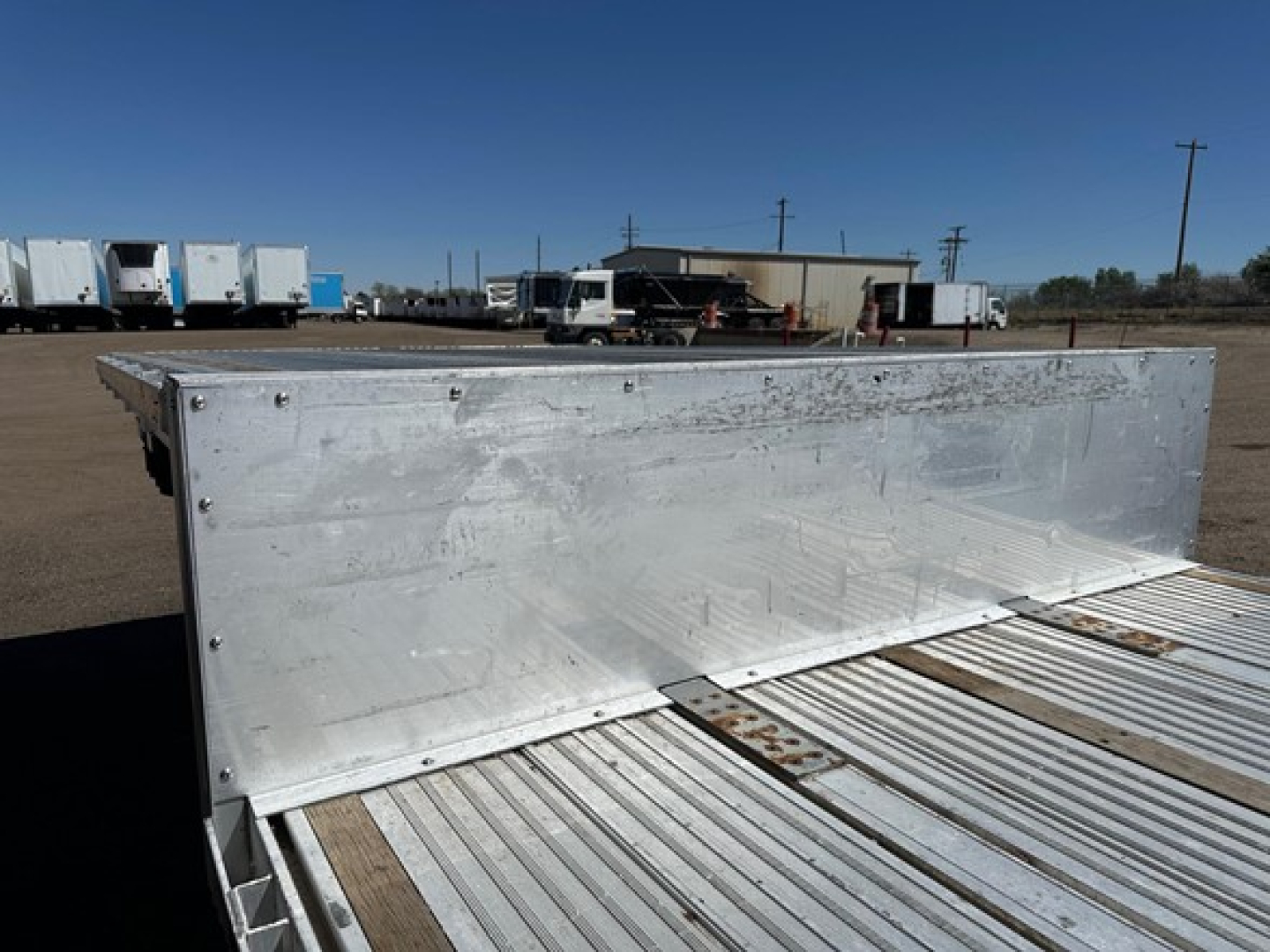 All-aluminum drop deck trailer with side panels, aluminum decking, and fastening rivets along the edge; visible wear and scuff marks on the aluminum surface.