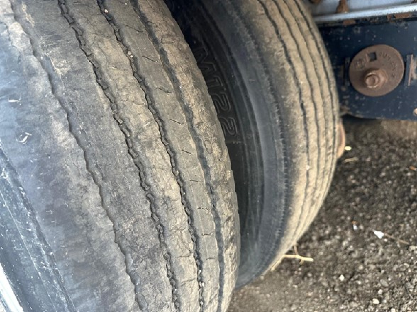 Trailer wheel assembly and tire sidewall close-up showing dual axles and weathered tread on all-aluminum drop deck trailer.