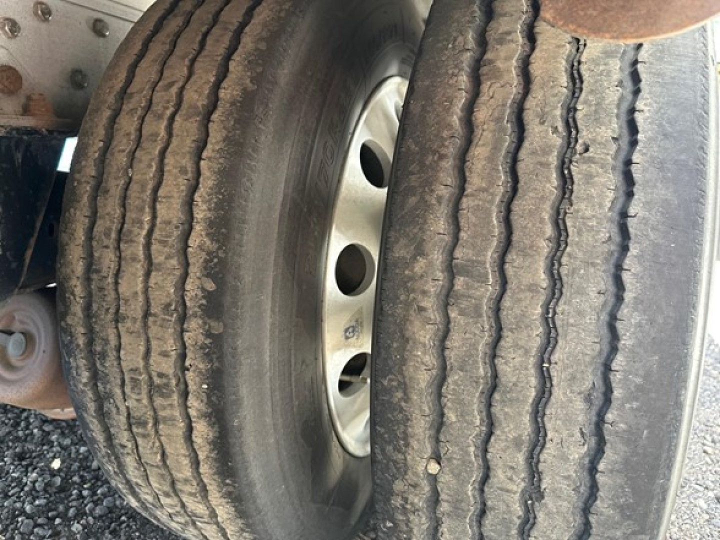 All-aluminum drop deck trailer wheel end showing dual tires and hub with circular holes.