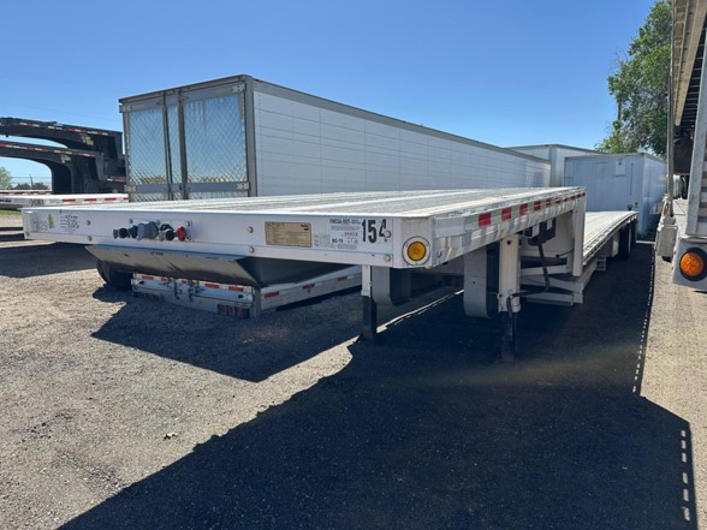 All-aluminum drop deck trailer showing serial plate and rear lighting; side rails and loading deck visible.