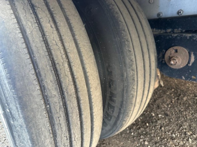 Rear dual tires and suspension on a used trailer with visible tire treads and a rusted bolt.