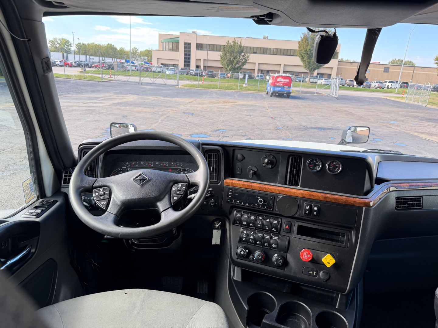 Interior view of a truck cab featuring a steering wheel, dashboard with wood trim, and control panel; digital gauges and cup holders visible.
