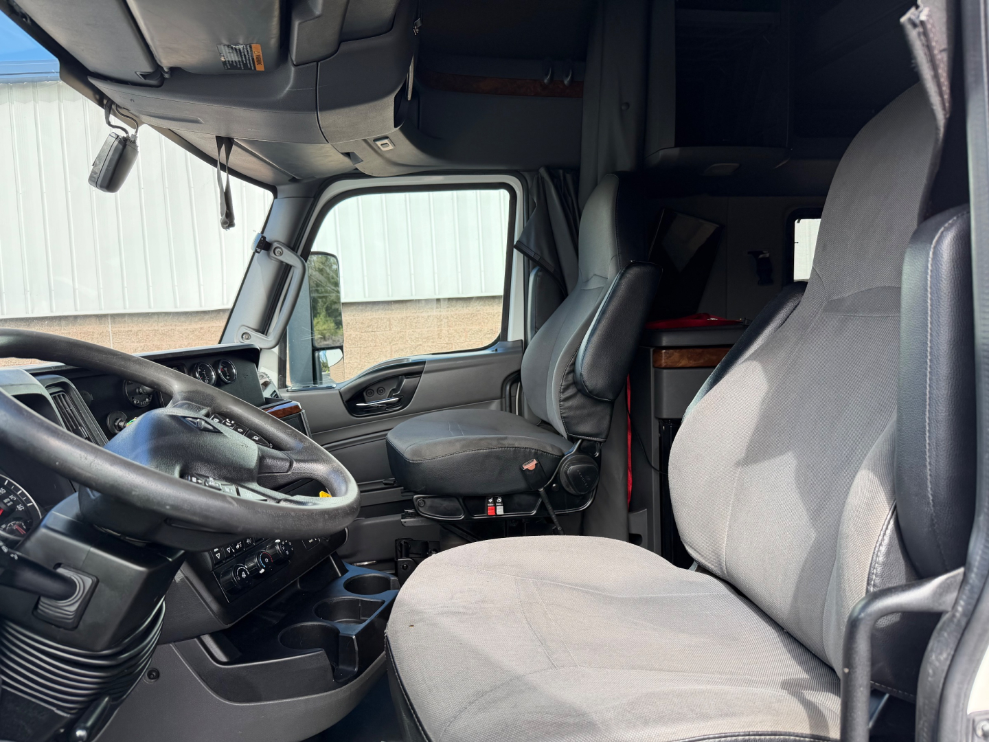 Interior of a 2021 International LT625 truck cab showing steering wheel, driver seat, passenger seat, dashboard, and overhead compartments with visible control panels.