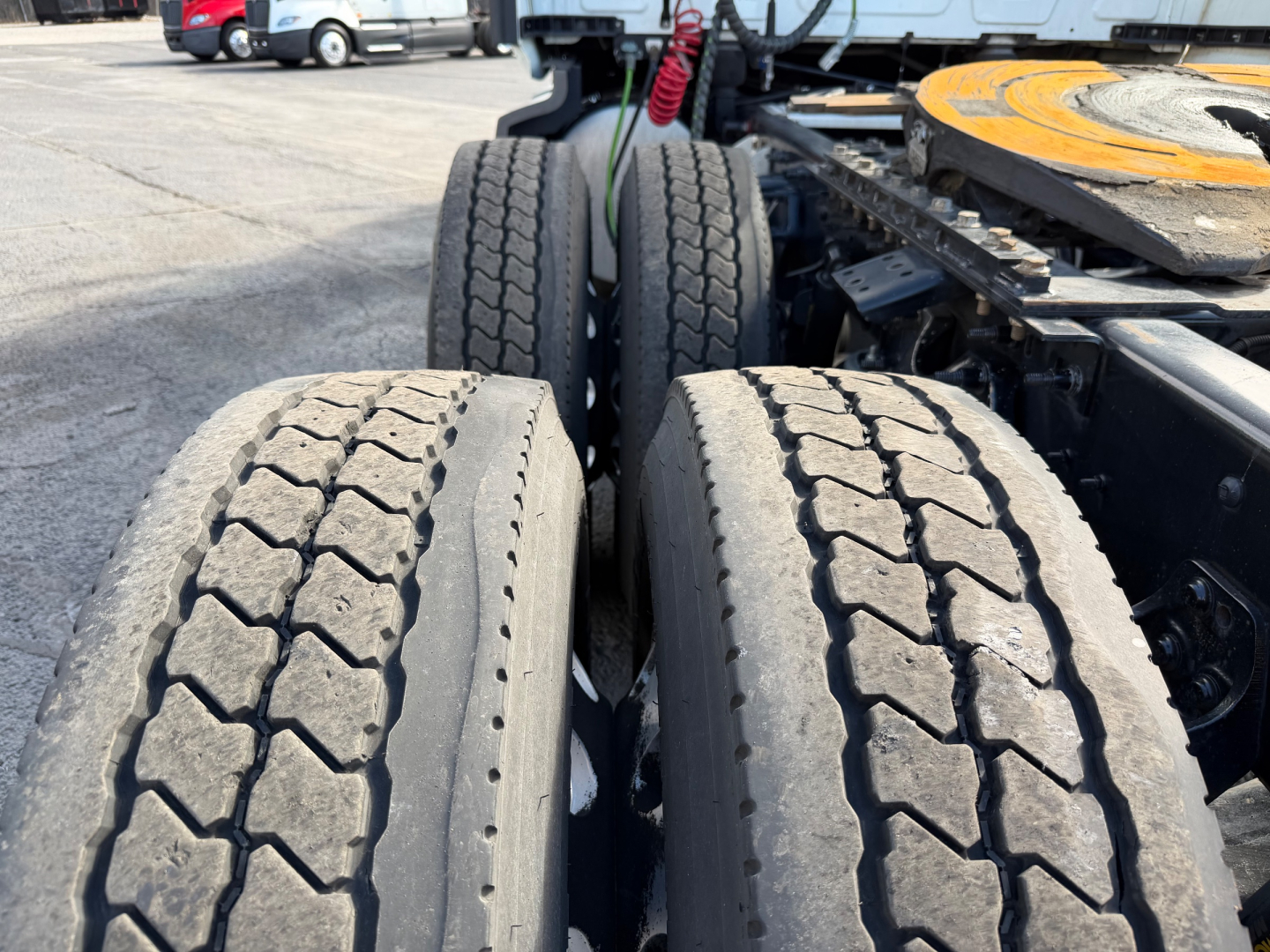 Truck rear axle dual tires with heavy tread showing suspension and fifth wheel plate in background