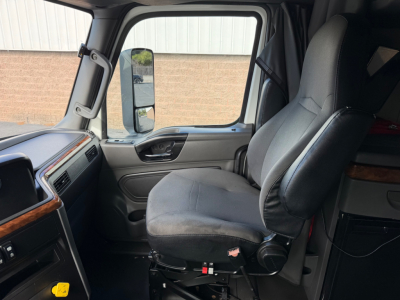 Truck cab interior showing driver's seat and passenger seat of a 2021 International LT625 with light gray cloth seats, dashboard with wood trim, and side window.
