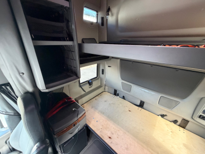 Interior of a truck cab showing sleeper berth area with overhead storage shelf and side panels. No legible brand text or numbers visible in the cabin area from this angle.
