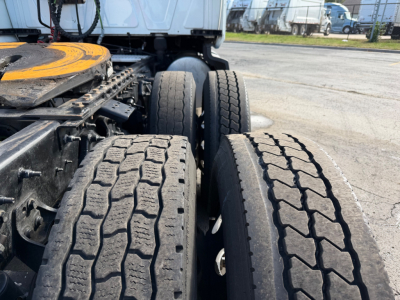 Dual rear axles and tires of a truck chassis with a yellow spare wheel cover visible; part of the fifth wheel area and cab in background.