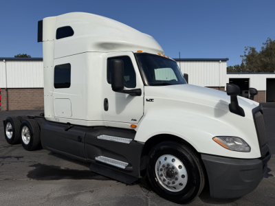 Truck side view showing International LT hood and cab with sleeper, fuel tanks, and triple rear axles. No visible text readable other than small badges on door and steps.