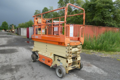 JLG 2646ES scissor lift in an outdoor lot, orange platform rails and tan base, view of rear/side with brand stickers and wheels visible.