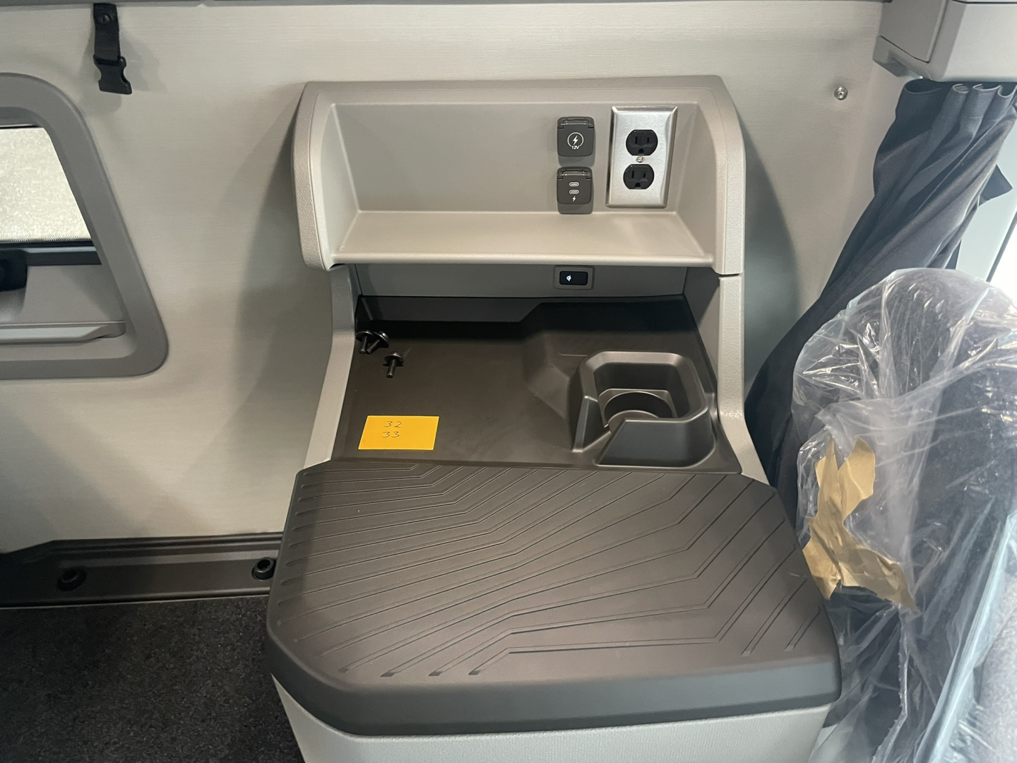  Volvo VNL64T860 sleeper cab area with electrical outlets, power ports, and a small storage shelf; seat covered in protective plastic visible.