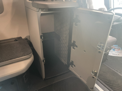 Truck cab interior showing a closed cabinet with two hinged doors and a small storage compartment beneath; light gray finish and textured panels.
