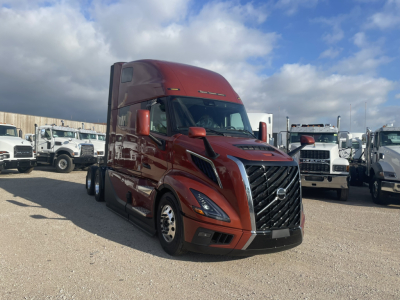 Volvo VNL64T860 sleeper tractor in red, front-left view, with grille and headlights visible, parked among other trucks.