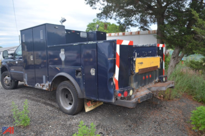 Rear view of a blue utility/service truck with multiple compartments and a yellow rear skid plate. Vehicle appears to be a Ford F-450 Super Duty with utility body and storage compartments.