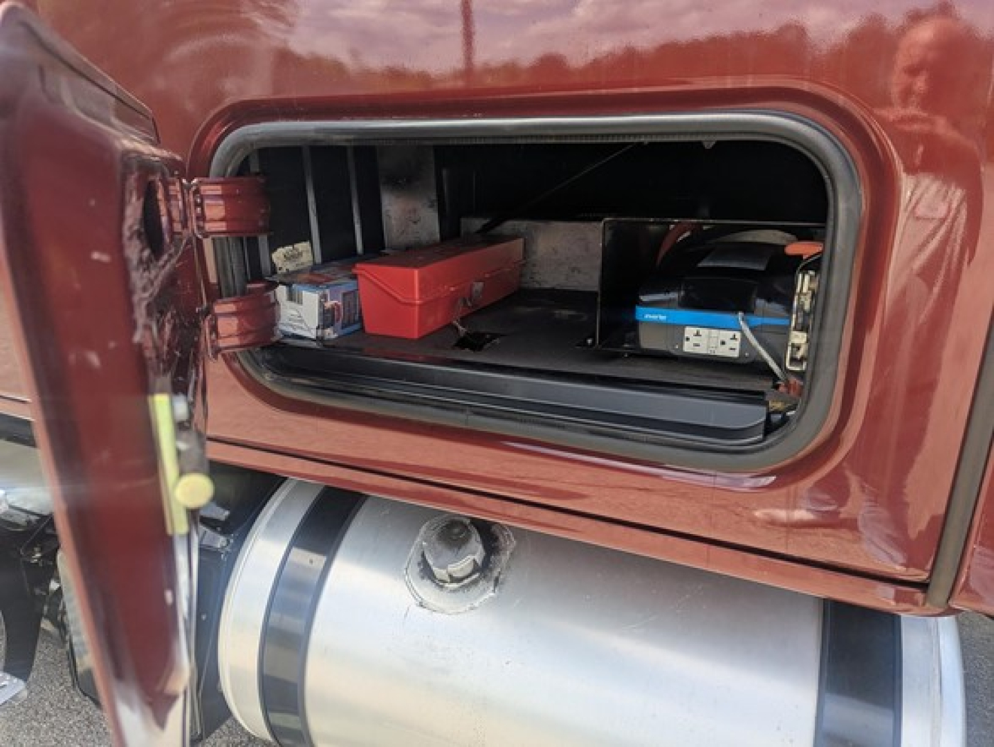 Freightliner Cascadia 126 cab storage compartment showing tools and battery boxes inside side access panel, fuel tank below.